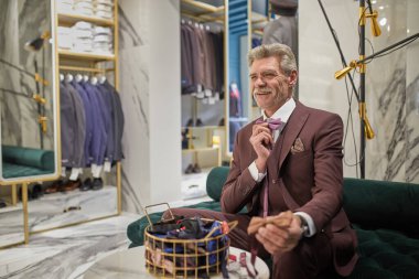 Gözlüklü olgun milyoner canlı bir toplantı için hazırlanıyor ve şık butikte dikkatlice papyon takıyor..