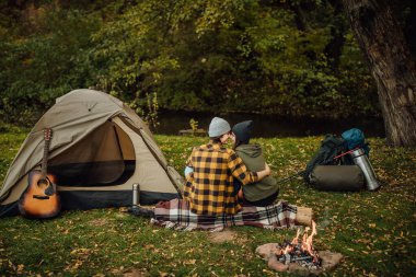 Güzel bir çift çadırın yanında oturmuş eğleniyor. Yakışıklı adam ve güzel kadın ormanda öpüşüyor..