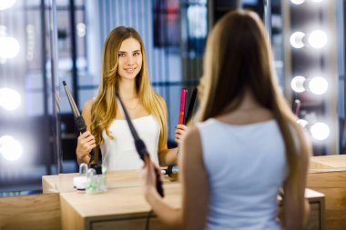 Genç ve güzel bir kız aynanın önüne kıvırcık maşayla sarılır..