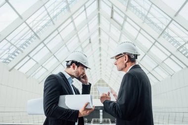 Yeni binaların projesi ve dizüstü bilgisayarıyla kask takan iki başarılı girişimci cam çatının yakınında kalıyor.
