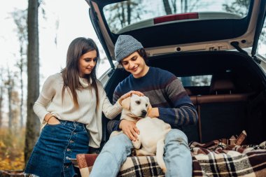 Sonbahar parkında köpekle birlikte arabada dinlenen genç bir çiftin fotoğrafı..