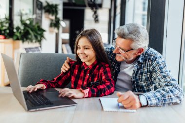 Torunuyla birlikte yetişkin bir adam tablet kullanıyor. Çocuğa video çağrısı yapıyor..