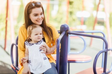 İki kız kardeş yaz parkında bir atlıkarıncada oturarak mutlu vakit geçirir..