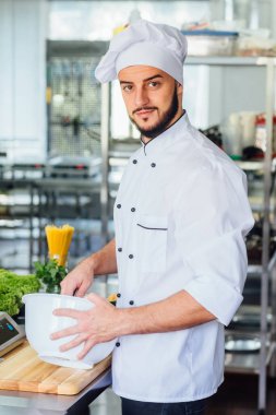 Pozitif genç aşçı iş yerinde elinde yemekle kameraya bakıyor..