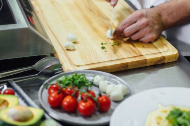 Erkek eli, tahta kesme tahtasında keskin bir bıçakla yumurta kesiyor ve mutfakta sebze salatası pişiriyor..