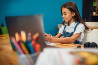 Neşeli küçük kız çocukları dizüstü bilgisayar kullanıyor, online e-öğrenim sistemi üzerinden çalışıyorlar..