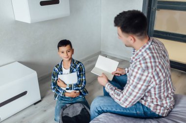 Baba, sabah yatak odasında kitap okurken oğlunun okula hazırlanmasına yardım et..