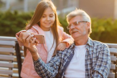 Büyükbaba ve torunun portresi bir bankta oturuyor ve akıllı telefonla konuşuyor..