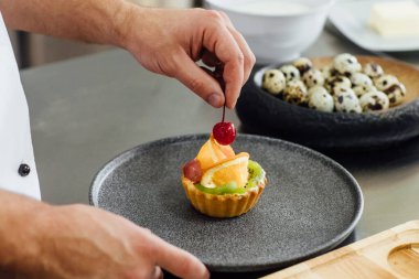 Fotoğrafı kapat. Aşçı mutfakta meyveli kek ve şeker süslüyor. Pasta, aşçılık, fırın, yemek ve insan konseptini dekore ediyor..
