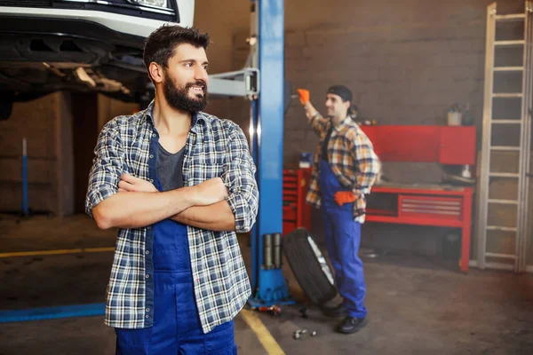 自動車工場を背景に同僚と目を合わせて腕を組んで制服を着た髭の男 — ストック写真