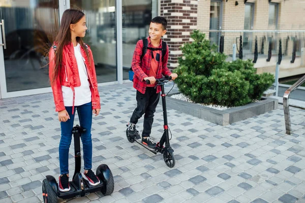 女孩和男孩一起骑着陀螺滑板车散步 他们互相微笑着 儿童的情绪 — 图库照片