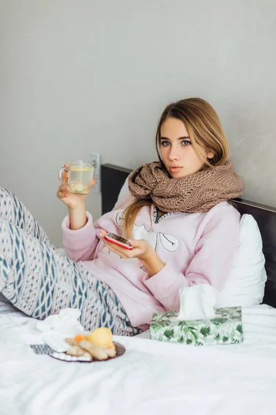 病人の不幸な若い女性は熱いお茶を飲みながらベッドに寝ている 家の電話で医者と話した後 — ストック写真