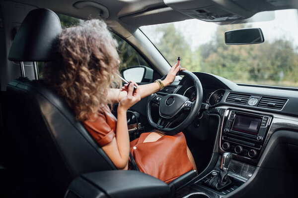 Portrait of cute blond fashion woman putting lipstick on using the car mirror.