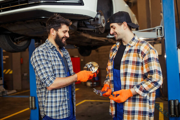 side view of two handsome workers looking at car detail in autoworkshop
