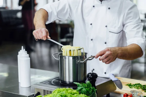 Close up photo, professional chief cook in white unifirm, boil spahhetti, kitchen equipment.