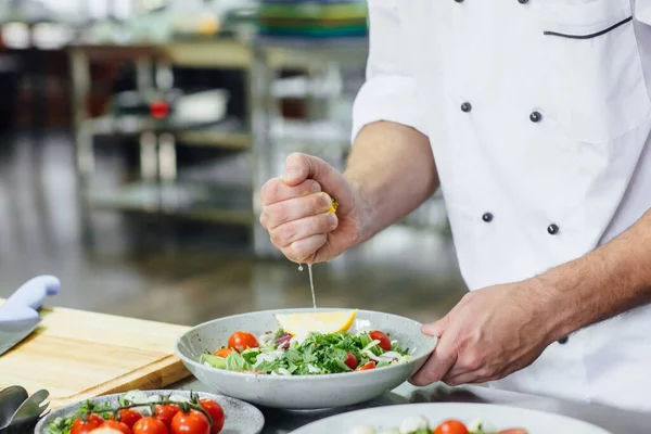 Aşçı şefi spagetti carbonara için limon sıkıyor, keskin bıçaklı ve mutfakta sebze salatası pişiriyor..