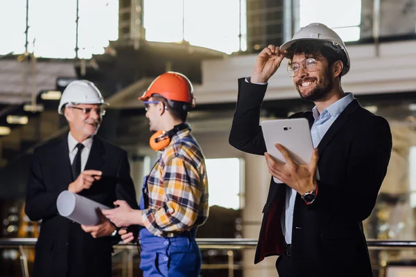 Business man meeting of architects and investors and foreman in modern factory, holding project in a laptop.
