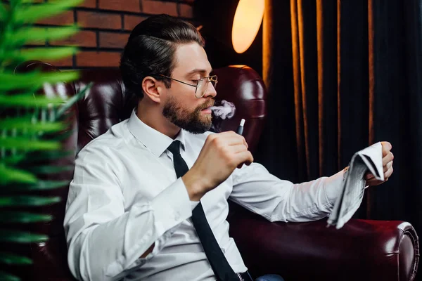 豪華な部屋で椅子に腰を下ろしているビジネスマン 家の中で煙草を吸ってるハンサムな男 — ストック写真