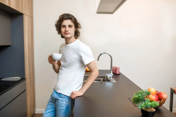 Beyaz Tişörtlü Yakışıklı Bir Erkek Portresi Mutfakta Sabah Kahvesi Içiyor — Stok fotoğraf