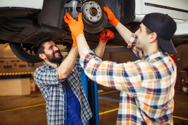 caucasian technicians working on tire of the lifted car in the modern service center