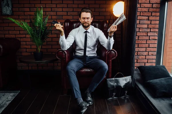 Przystojny Biznesmen Trzyma Swój Smartfon Gazetę Siedząc Fotelu — Zdjęcie stockowe