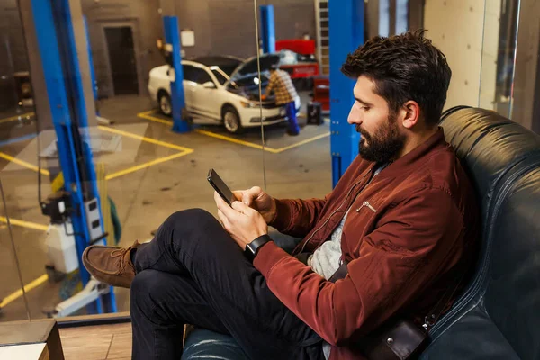 Seriózní Muž Pomocí Smartphonu Zatímco Technik Opravuje Své Auto Garáži — Stock fotografie