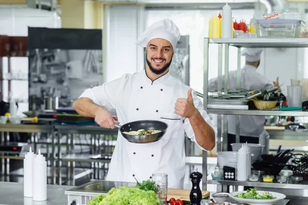 若い髭を生やした笑顔の男性シェフキッチンで食べ物を飾る 大丈夫サイン — ストック写真