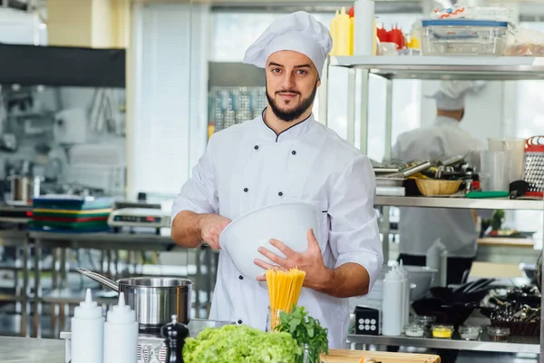 人々のコンセプト 幸せな男性シェフは現代的で白いレストランキッチンで調理します — ストック写真