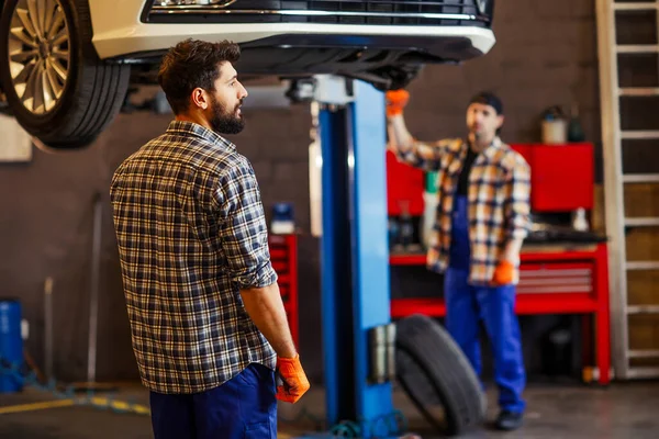 Dwóch Mechaników Pracujących Razem Nad Podnoszonym Samochodem Warsztacie — Zdjęcie stockowe