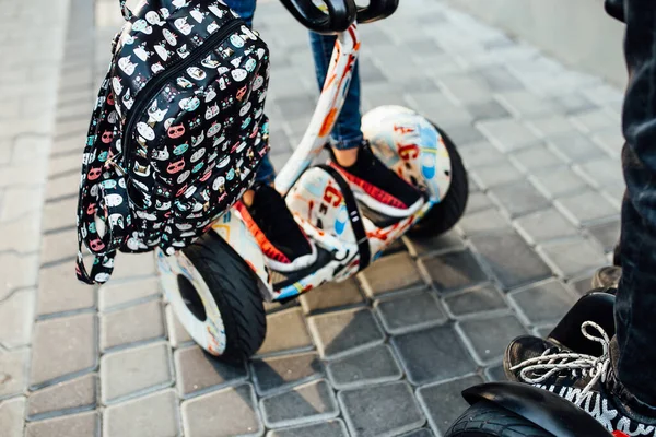 Couple legs riding electric mini hoverboard in park, backpack on hands. Close up leg photo.
