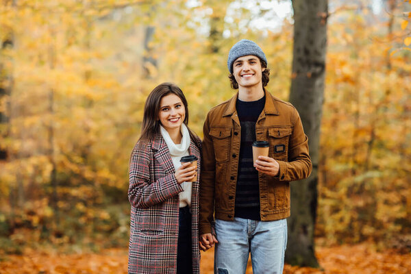 Family and hot autumn drink concept. Couple in love with scarves sits in park holding cups of tea or coffee.