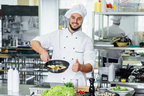 Young, bearded and successful smiling male, cook chef garnishing food in kitchen, okay sign.