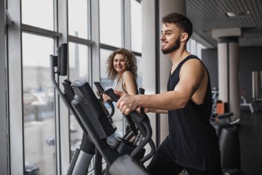 Siyah spor salonunda erkek ve kadın eliptik yürütme eğitmeni aerobik eğitimi alıyor..