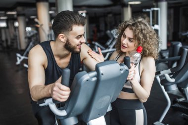 Eğitimden sonra bir erkek ve bir kadın konuşuyor. Spor salonundaki spor malzemelerinin üzerine oturmuş dinlenen bir adam..