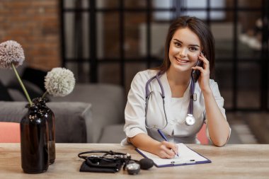 Genç, güzel bir bayan doktor kameraya bakıyor ve gülümsüyor..