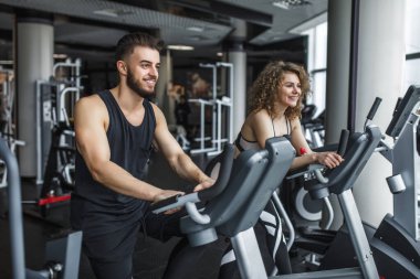 Çekici genç kadın ve spor salonunda koşu bandında koşan antrenörü. Spor salonunda koşan zayıf kız, kameraya gülümsüyor. Sağlıklı yaşam tarzı kavramı, kardiyo eğitimi.