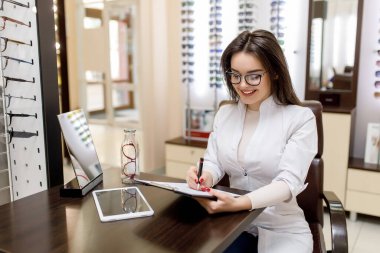İlaç, eczane ve optik. Beyaz cüppeli bir kadın doktor ya da eczacı portresi optik klinikte bir tarif yazar..