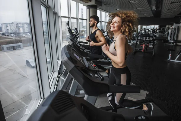 Running time, photo of young sports couple making cardio workout in modern gym.