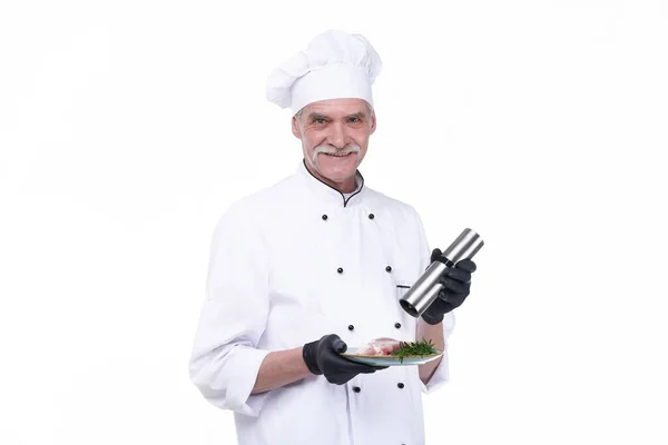 Cook with happy face, elderly chef male holds steak meat and pepper. Man with beard isolated on white background.