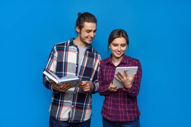 Mavi arka planda poz veren mutlu evli çift mavi arka planda, dizüstü bilgisayarlarını ve kitaplarını ellerinde tutuyorlar..