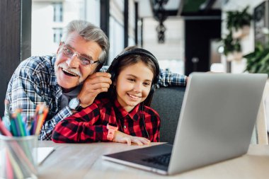 Torunuyla yaşlı komik bir adam kulaklıkla oynamak için dizüstü bilgisayar kullanıyor..
