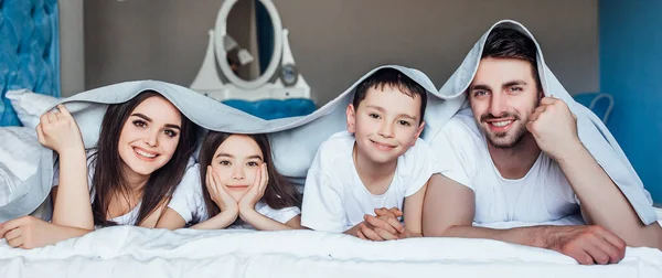 年轻的家庭一起睡在父母的床上 盖着毯子 — 图库照片