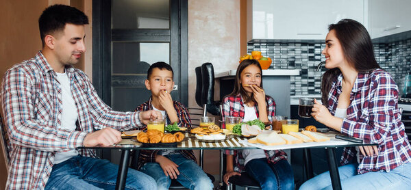 Cheerful parents with children during breakfast at home, four person sitting and eating food.