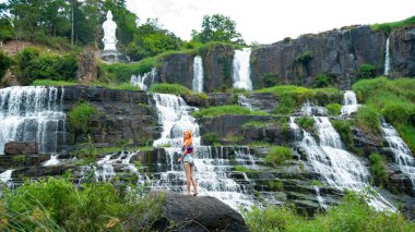 Güzel kızıl saçlı kız Vietnam 'da muhteşem şelalenin yanında kalıyor. Uzun kızıl saçlı gezgin kız güzel Pongour şelalesine bakıyor..