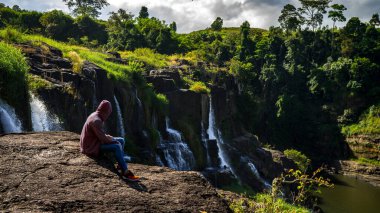 Da Lat şehrinde şelalenin yanında kalan genç adamlar. Uzun kızıl saçlı gezgin çocuk güzel Pongour şelalesine bakıyor..