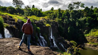 Da Lat şehrinde şelalenin yanında kalan genç adamlar. Uzun kızıl saçlı gezgin çocuk güzel Pongour şelalesine bakıyor..
