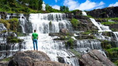 Da Lat şehrinde şelalenin yanında kalan genç adamlar. Uzun kızıl saçlı gezgin çocuk güzel Pongour şelalesine bakıyor..