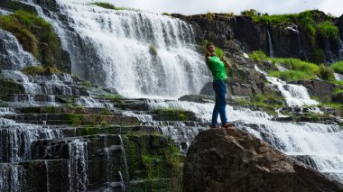 Da Lat şehrinde şelalenin yanında kalan genç adamlar. Uzun kızıl saçlı gezgin çocuk güzel Pongour şelalesine bakıyor..
