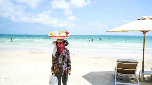 An elderly Vietnamese woman walks on the beach with a traditional don ganh wicker fruits basket.Street food vendor in Phu Quoc island.