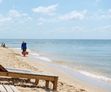 Yaşlı Vietnamlı bir kadın geleneksel Don Ganh hasır meyve sepetiyle sahilde yürüyor. Geleneksel Vietnam şapkası şapkasıyla Phu Quoc adasındaki sokak yemekleri satıcısı..